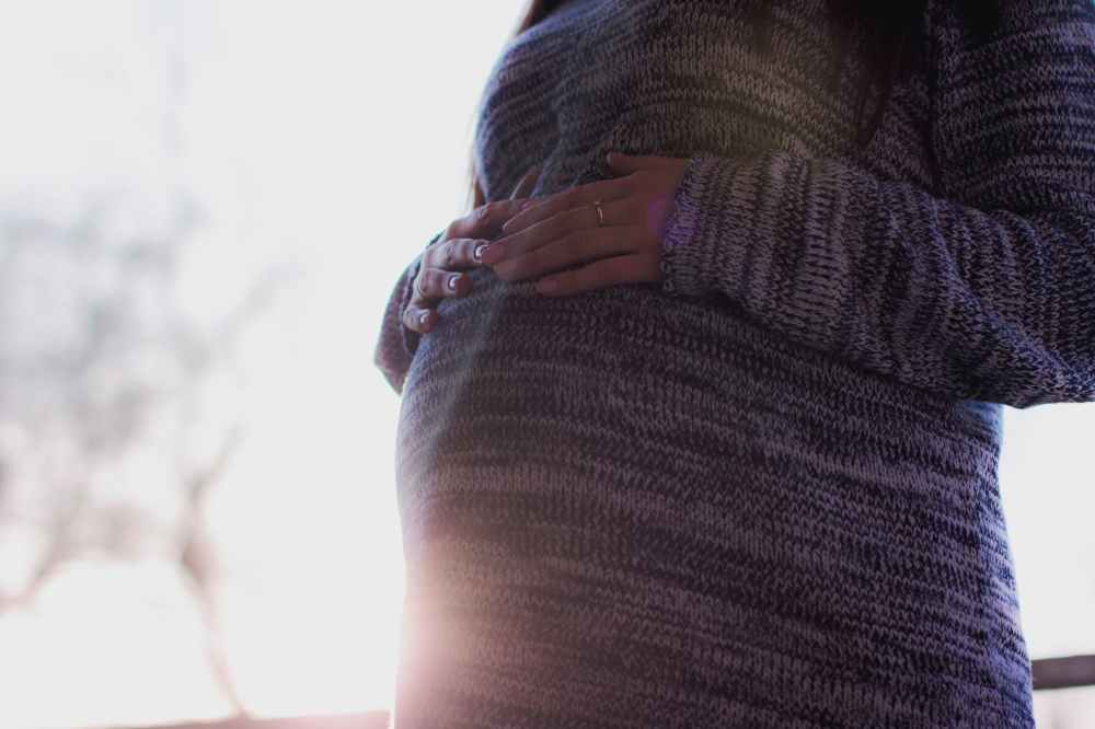 pregnant woman wearing marled gray sweater touching her stomach